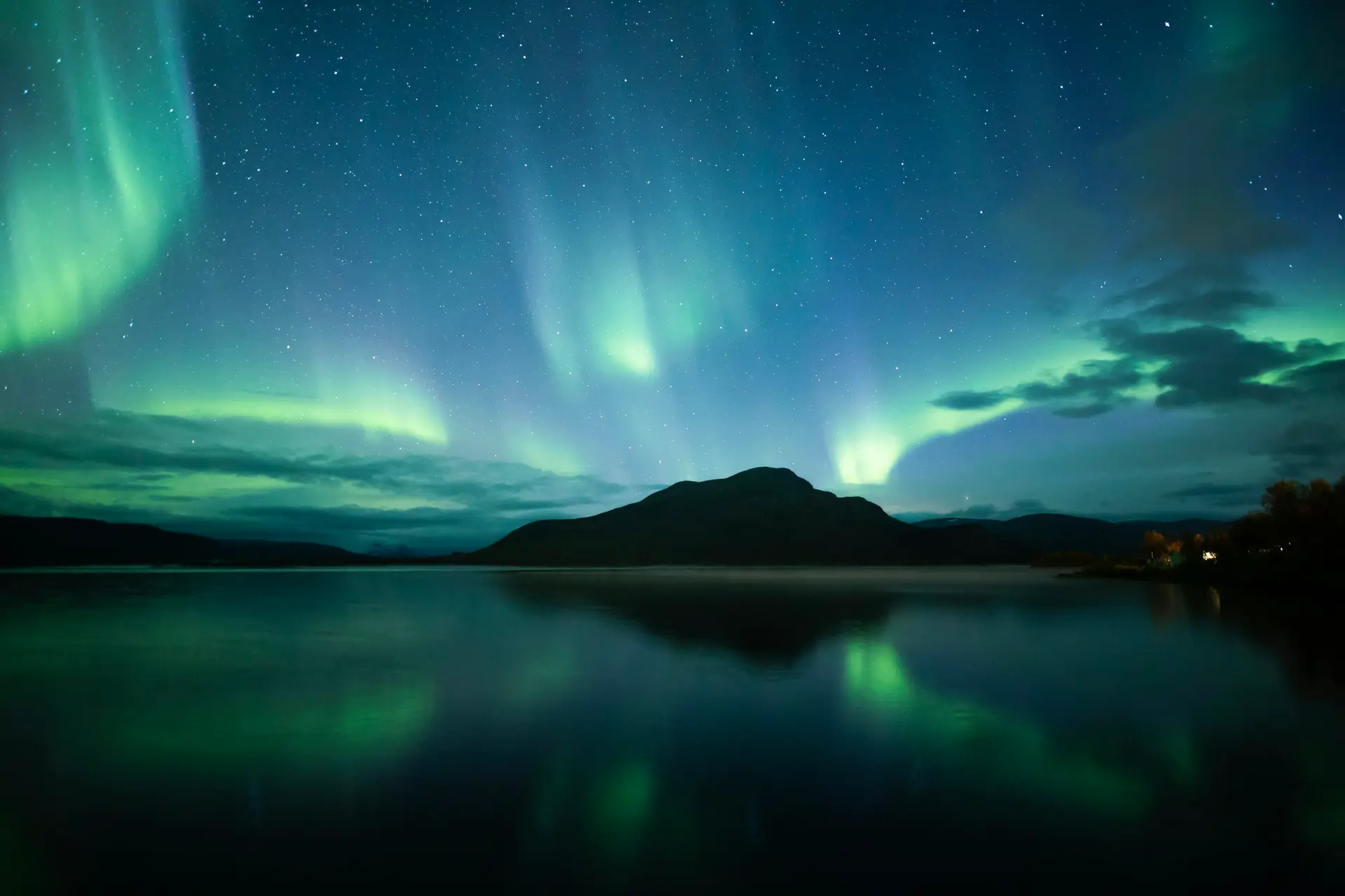 Green aurora over a fell and a still lake in Kilpisjärvi, Finnish Lapland